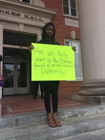 Student in protest of banner defacement holds sign at Sikes Hall.