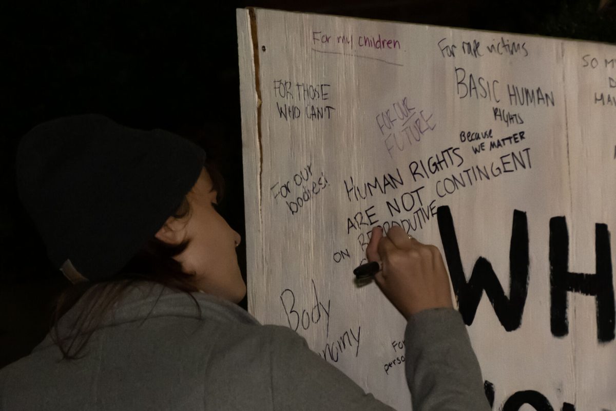 A student writes on a sign that asks "WHY DO YOU FIGHT?"