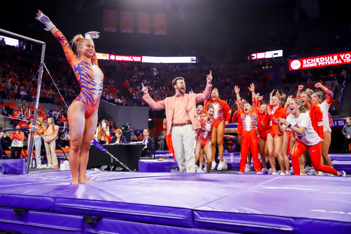 Lilly Lippeatt lands her first bar routine in the Tigers inaugural meet while teammates and assistant head coach Erik Lewis cheer by her side.