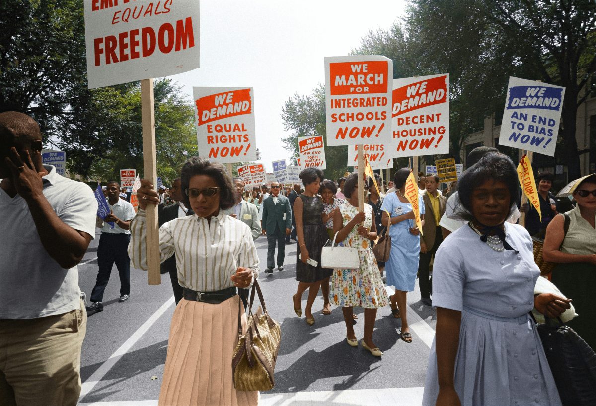 Demonstrators walk along a street holding signs demanding the right to equal civil rights at the March on Washington.